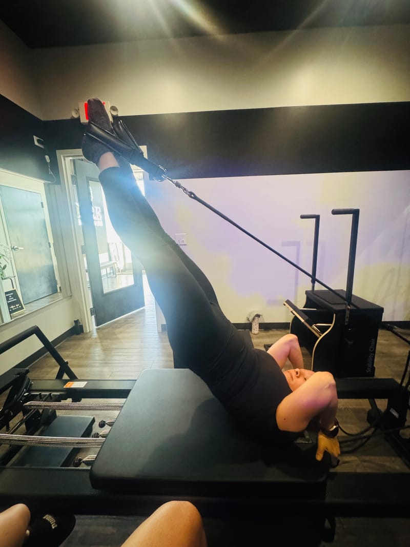 Leg press in straps on the Reformer during private training at Core Ambitions